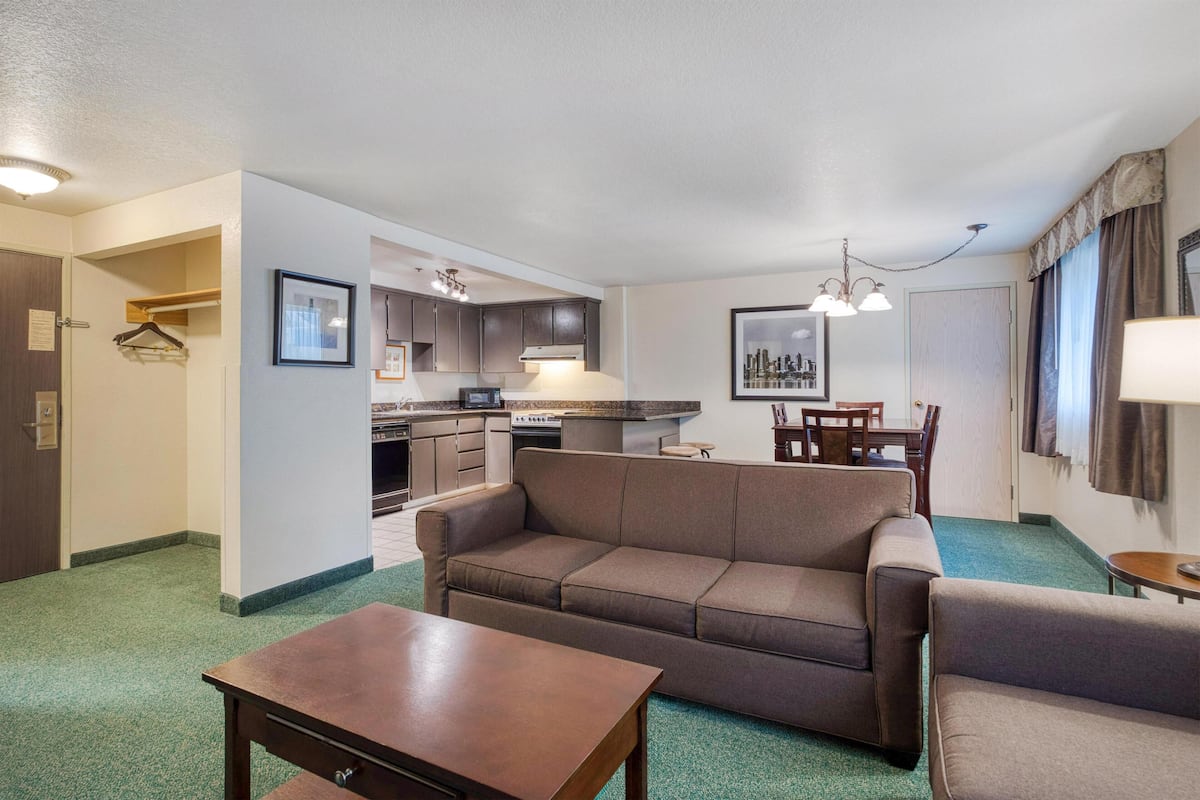 A compact hotel room with a kitchenette, a sofa, a dining table, and a small coffee table.
