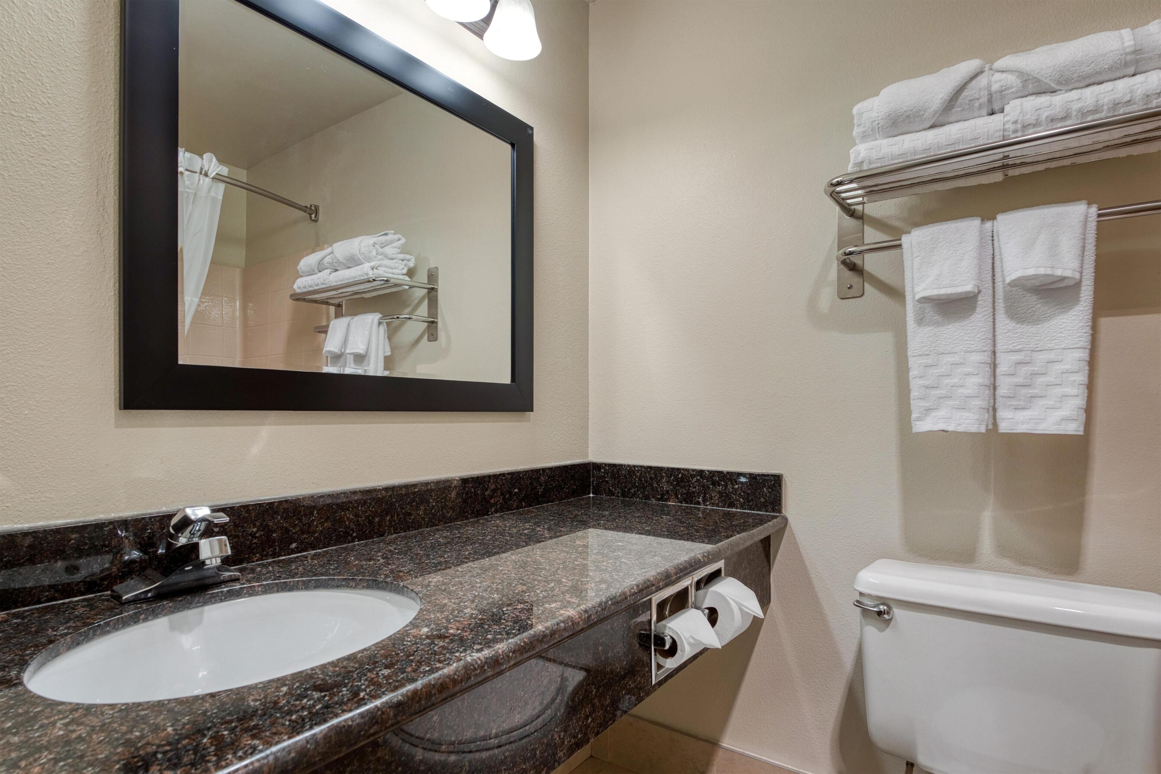 A bathroom with a granite countertop sink, a mirror, a towel rack, and a toilet.