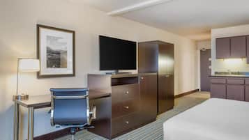 Une chambre d’hôtel comprenant un lit, un bureau avec une chaise, une télévision, une armoire et une petite kitchenette.