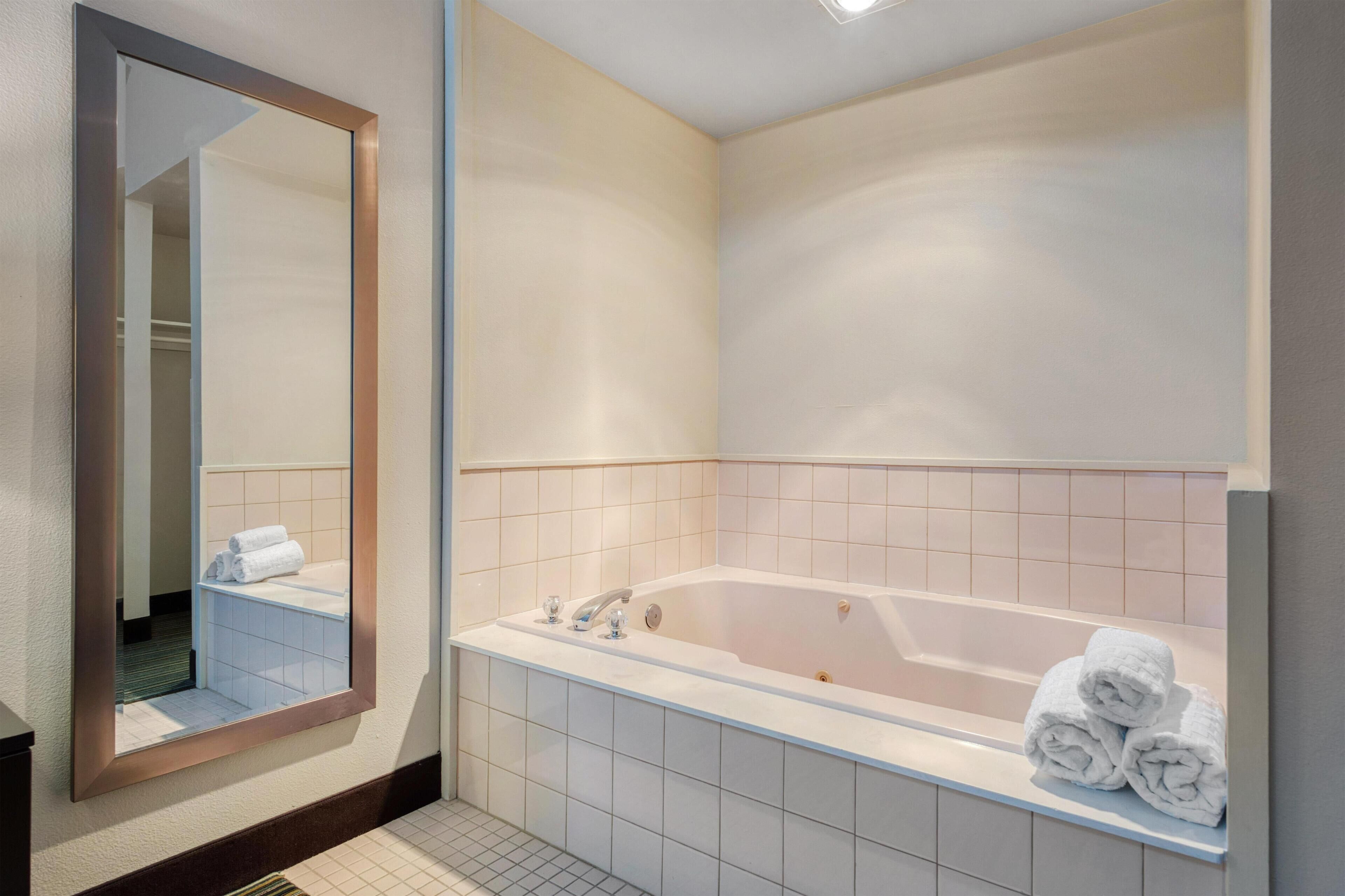 A modern bathroom with a large bathtub, a mirror, and neatly folded towels.