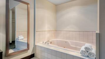 A modern bathroom with a large bathtub, a mirror, and neatly folded towels.