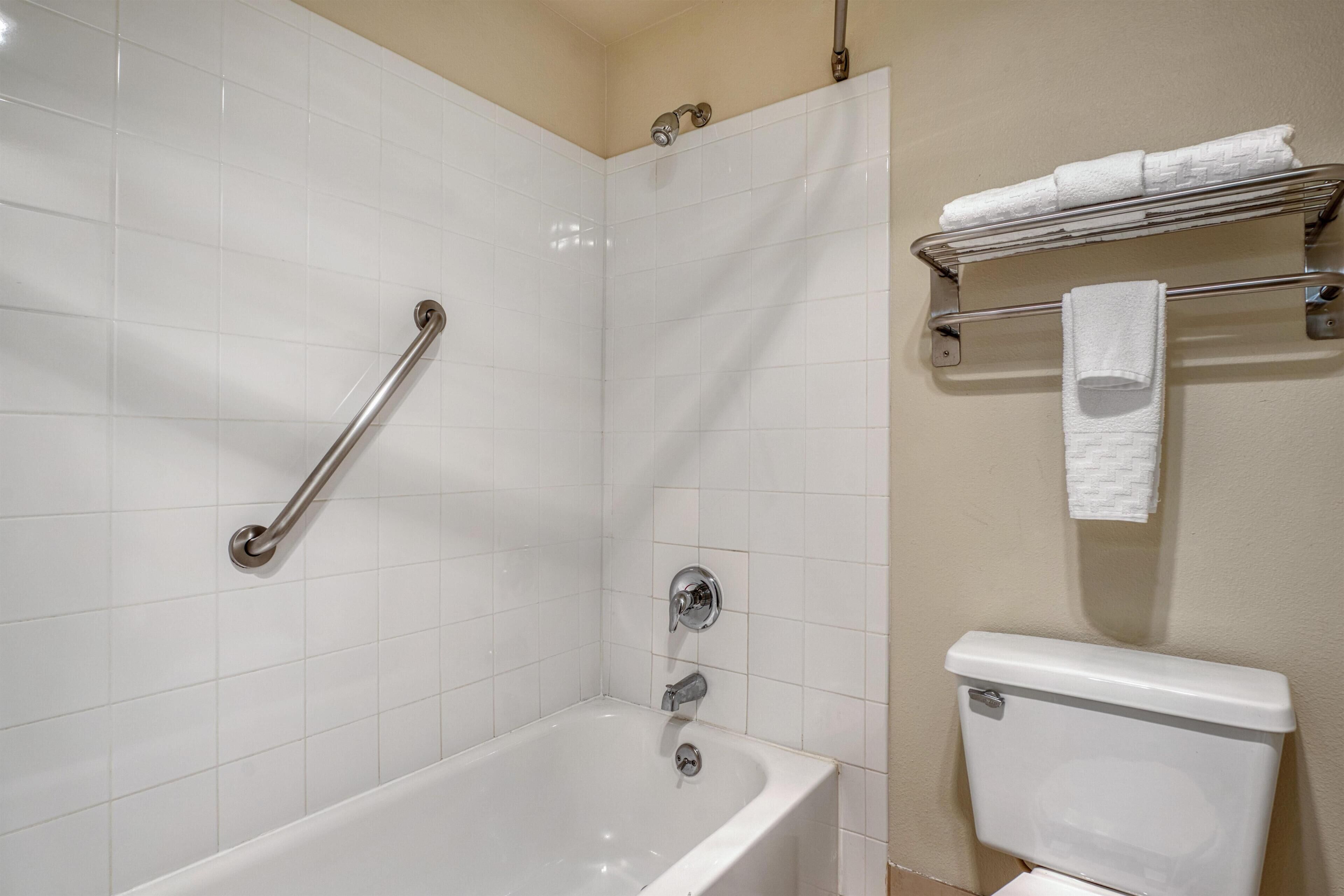 A bathroom with a bathtub, a toilet, a handrail, and a towel rack.