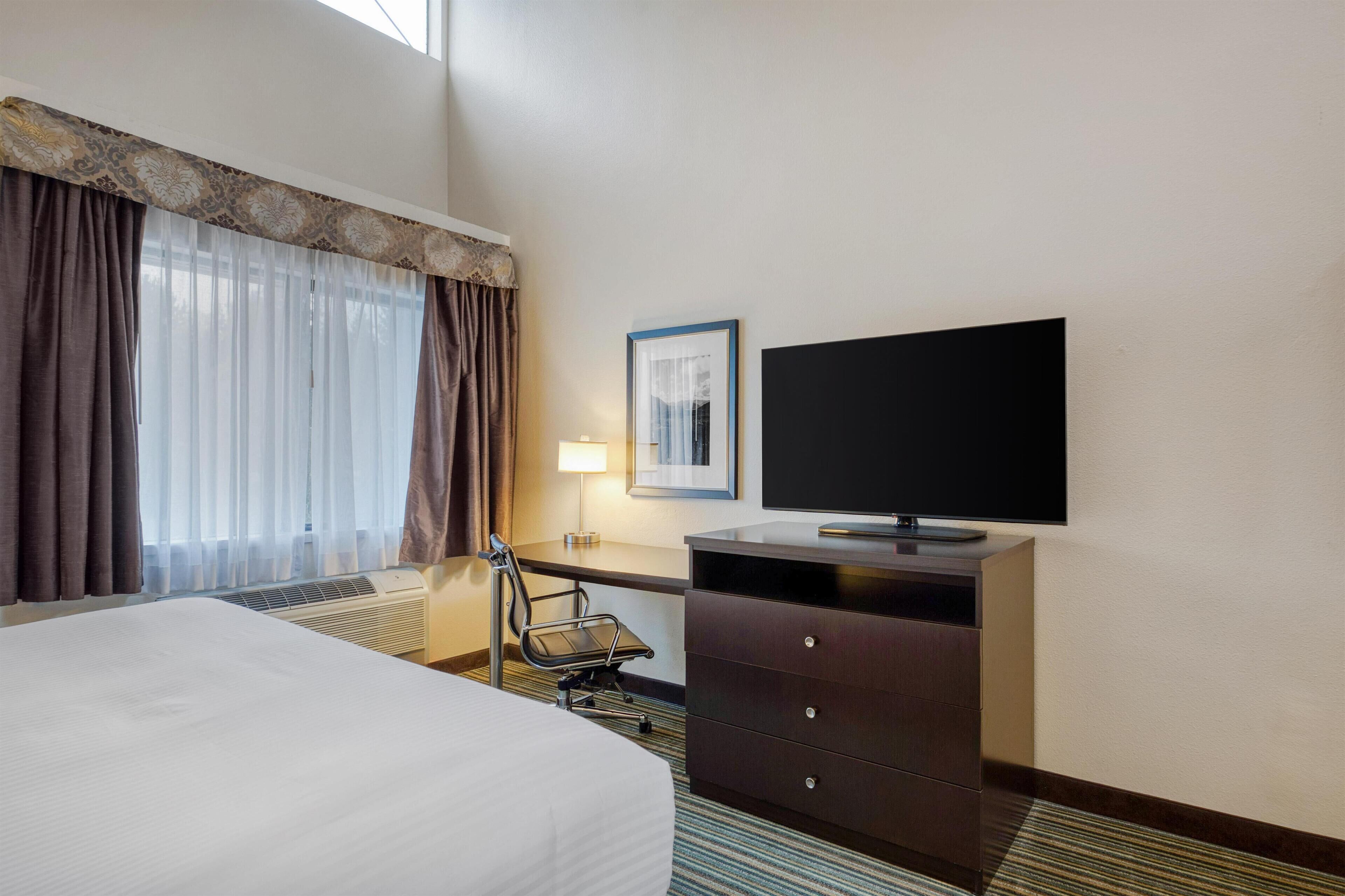 Una habitación de hotel con una cama, un escritorio, una silla, un televisor y una ventana con cortinas.
