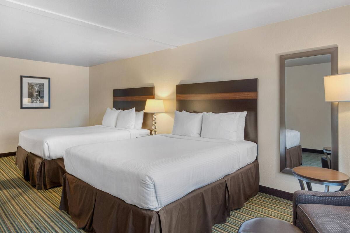 A hotel room with two beds, a small table, a chair, and a large mirror.