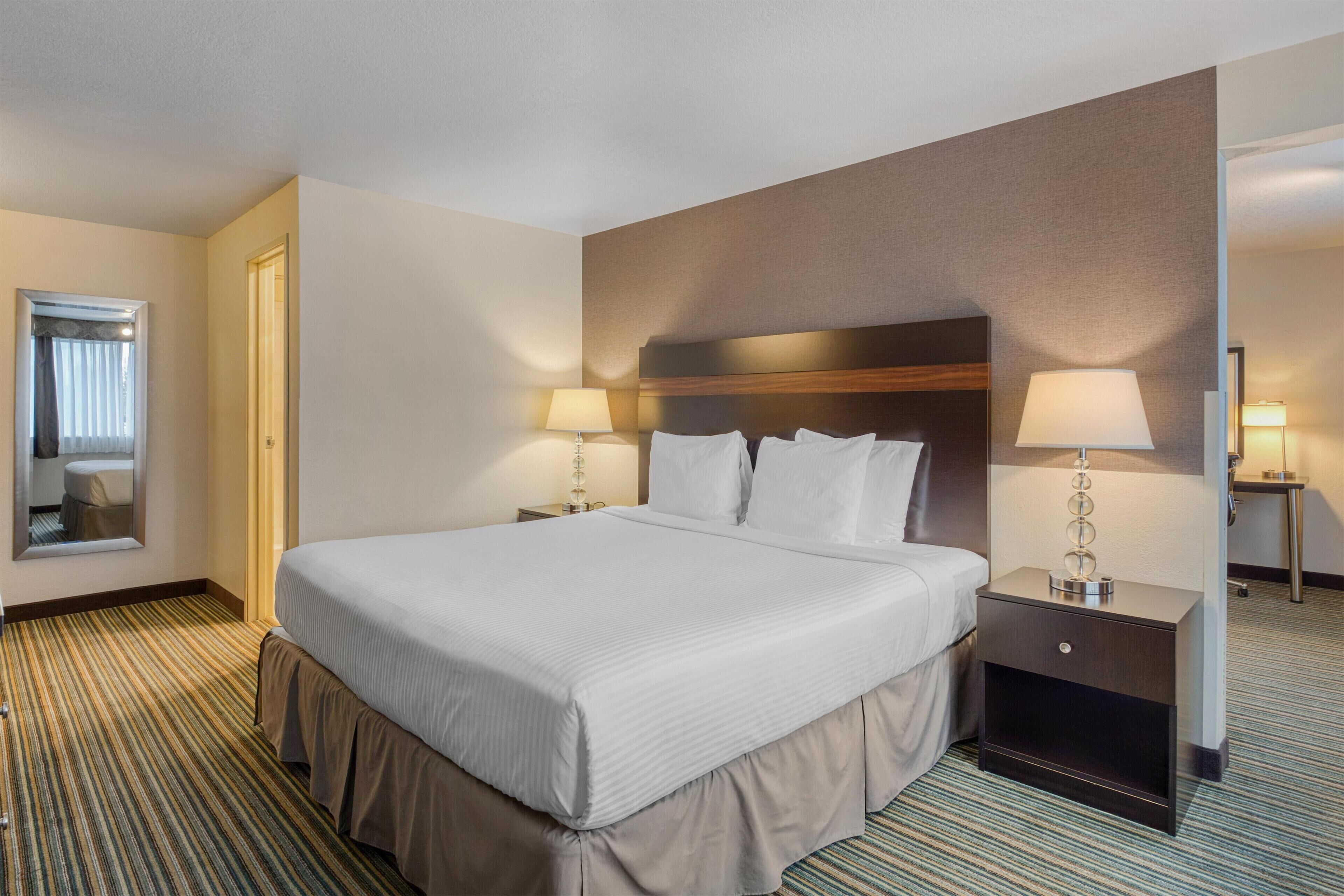 Une chambre d’hôtel avec un grand lit, deux tables de chevet avec des lampes, un miroir et une moquette à rayures.