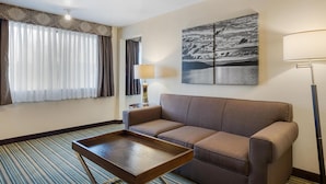 A hotel room with a sofa, a small table, a lamp, and a large landscape painting on the wall. - Best Western Alderwood (Lynnwood)