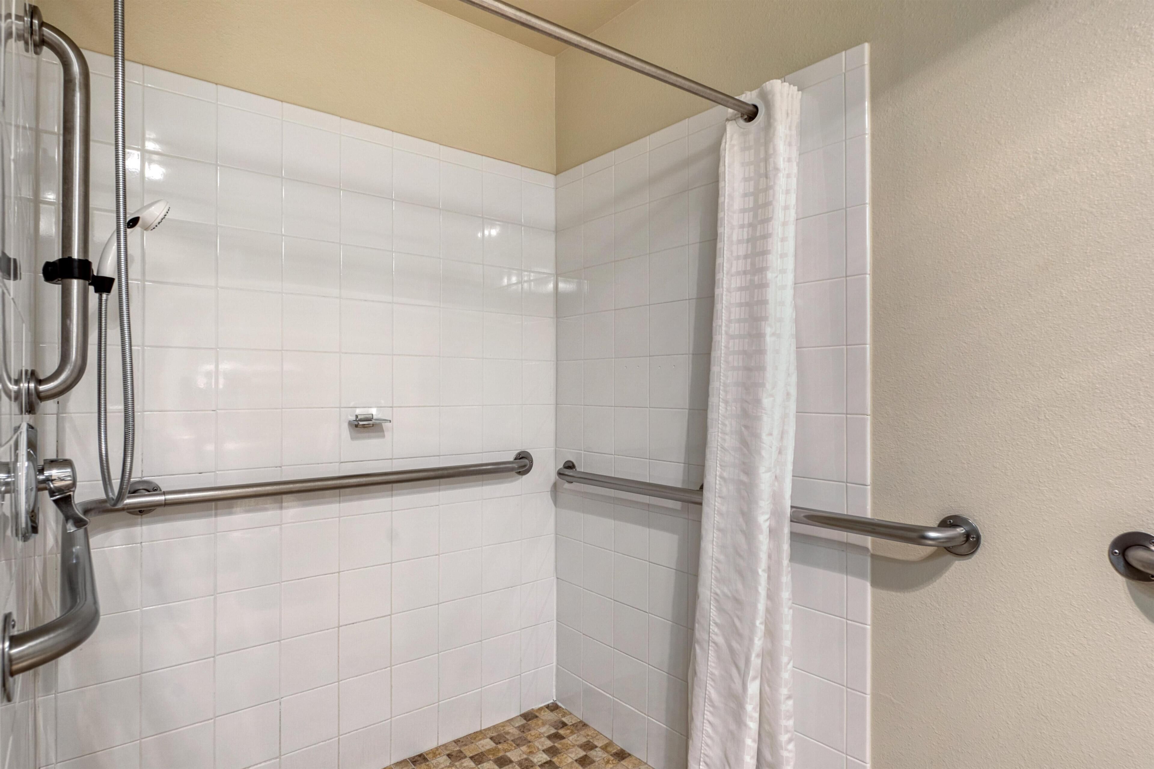 A shower area with white tiled walls, a metal grab bar, and a showerhead.
