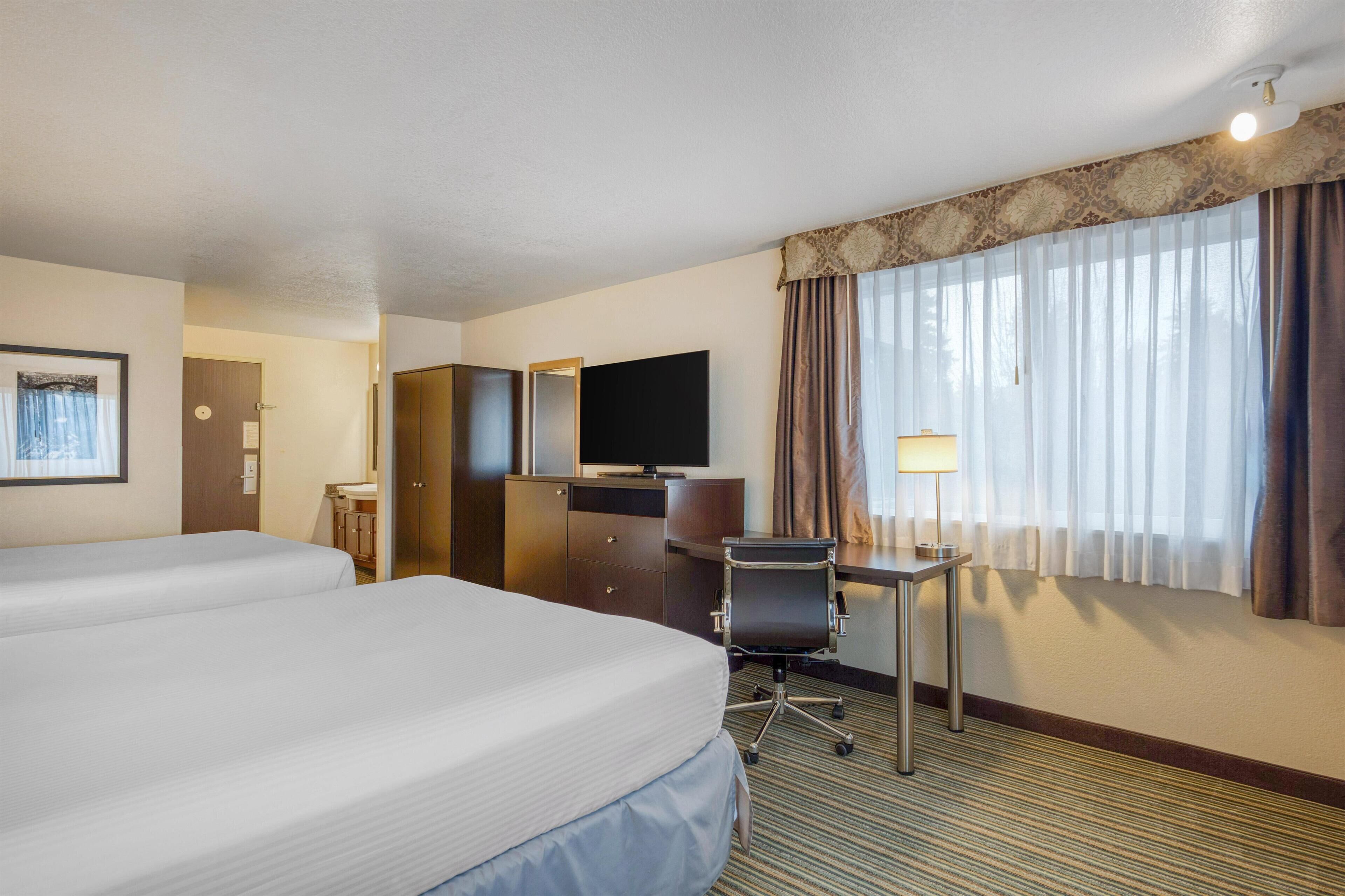 A hotel room with two beds, a desk, a chair, a television, and a window with curtains.