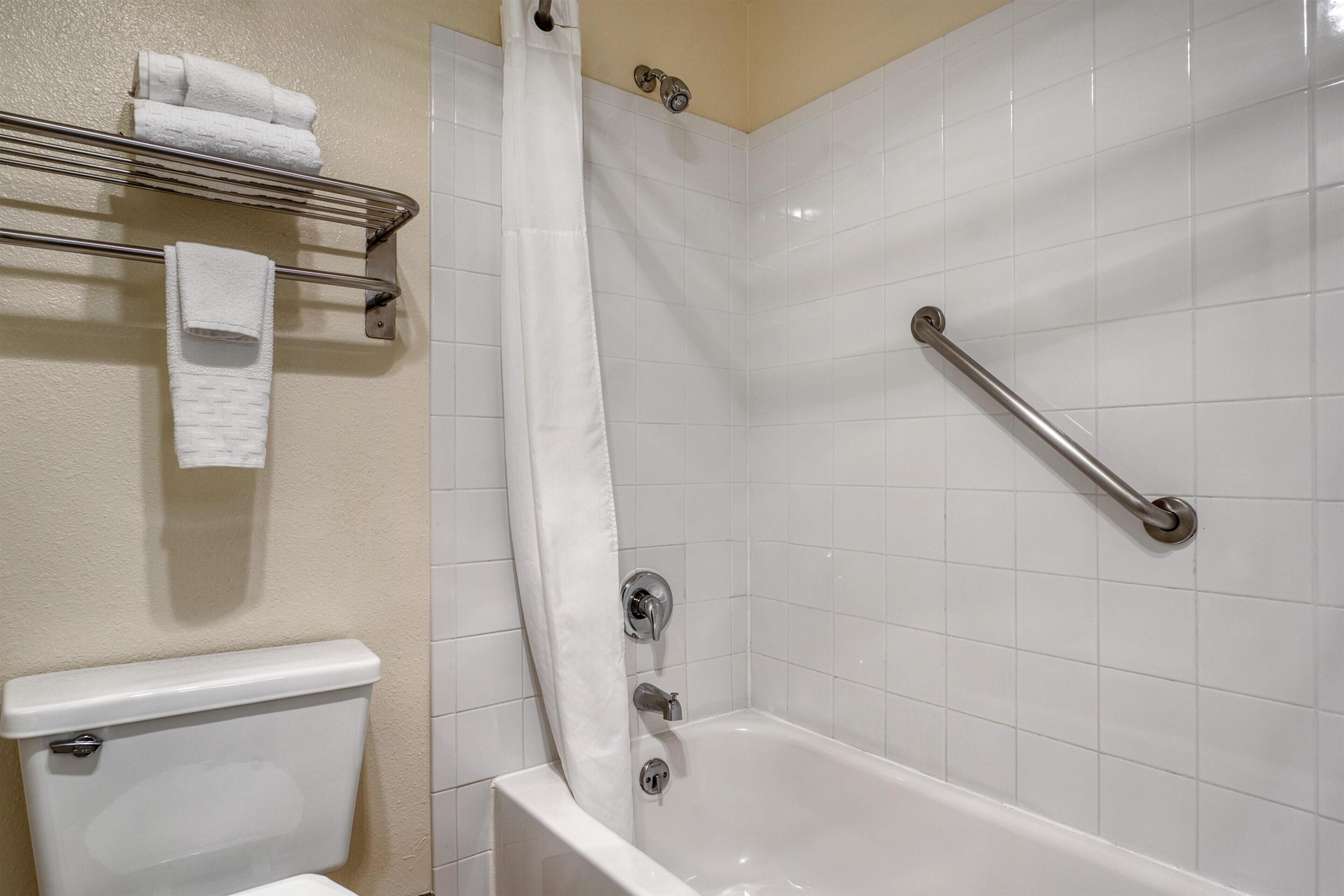 A bathroom with a white bathtub, a shower curtain, a grab bar, and a towel rack with folded towels.