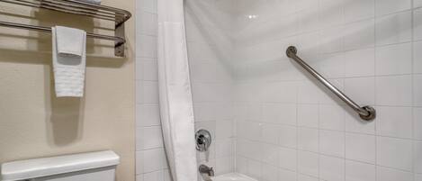 A bathroom with a white bathtub, a shower curtain, a grab bar, and a towel rack with folded towels.