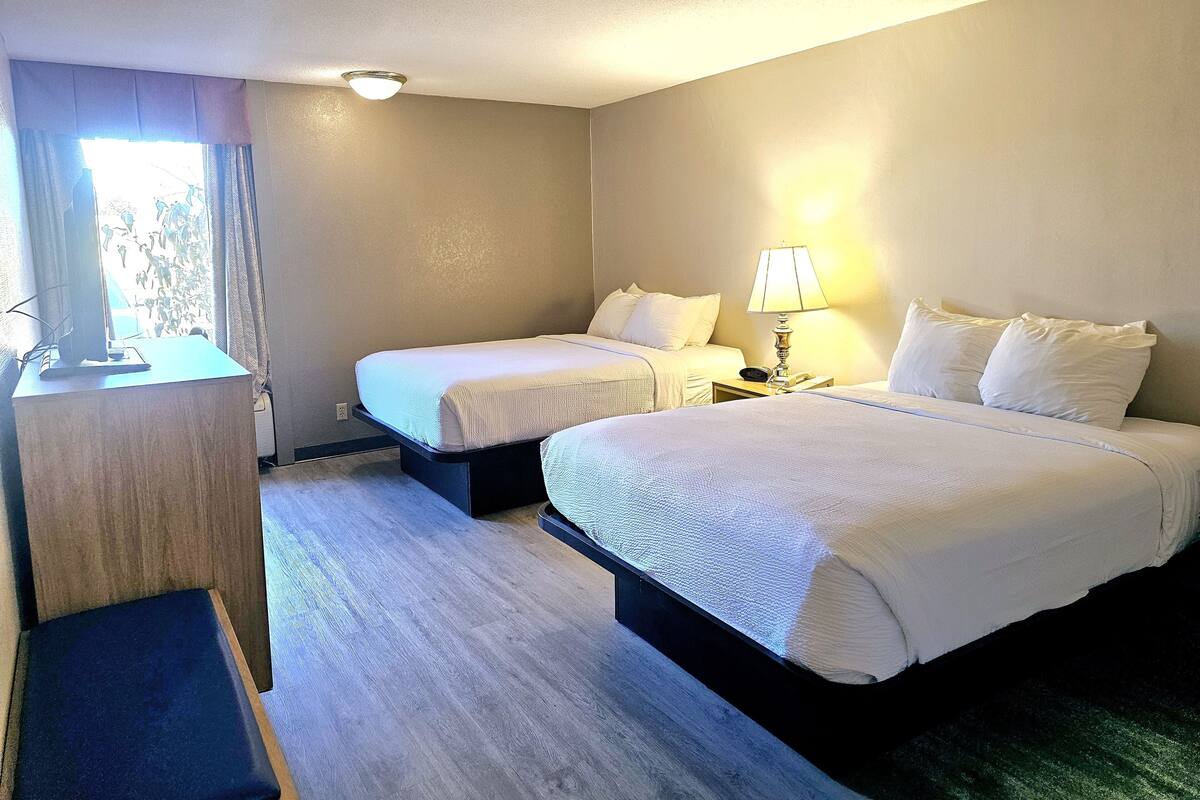A hotel room with two beds, a desk, a lamp, and a window with curtains.
