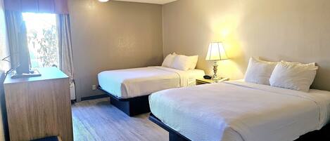 A hotel room with two beds, a desk, a lamp, and a window with curtains.