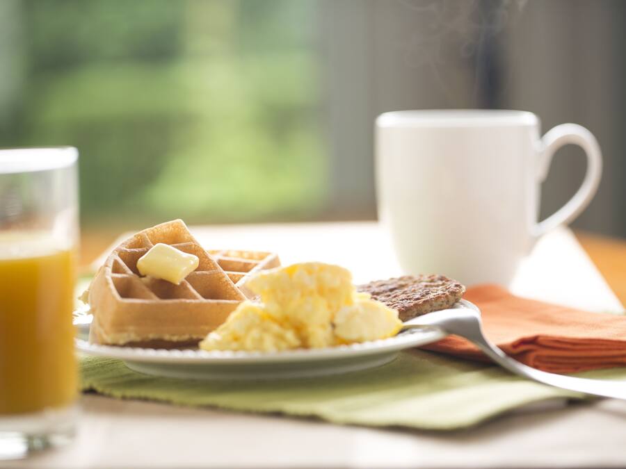 A breakfast setting with waffles, scrambled eggs, toast, and a cup of coffee on a table.