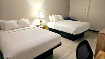 Quarto de hotel com duas camas, uma mesa, uma cadeira, um abajur e telefone na mesinha de cabeceira.