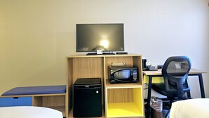 Habitación de hotel con cama, escritorio con computadora, silla, televisor sobre una estantería de madera y microondas.
