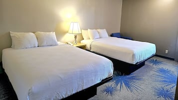 Hotellihuone, jossa on kaksi sänkyä, yöpöytä lampun kanssa ja sininen matto.