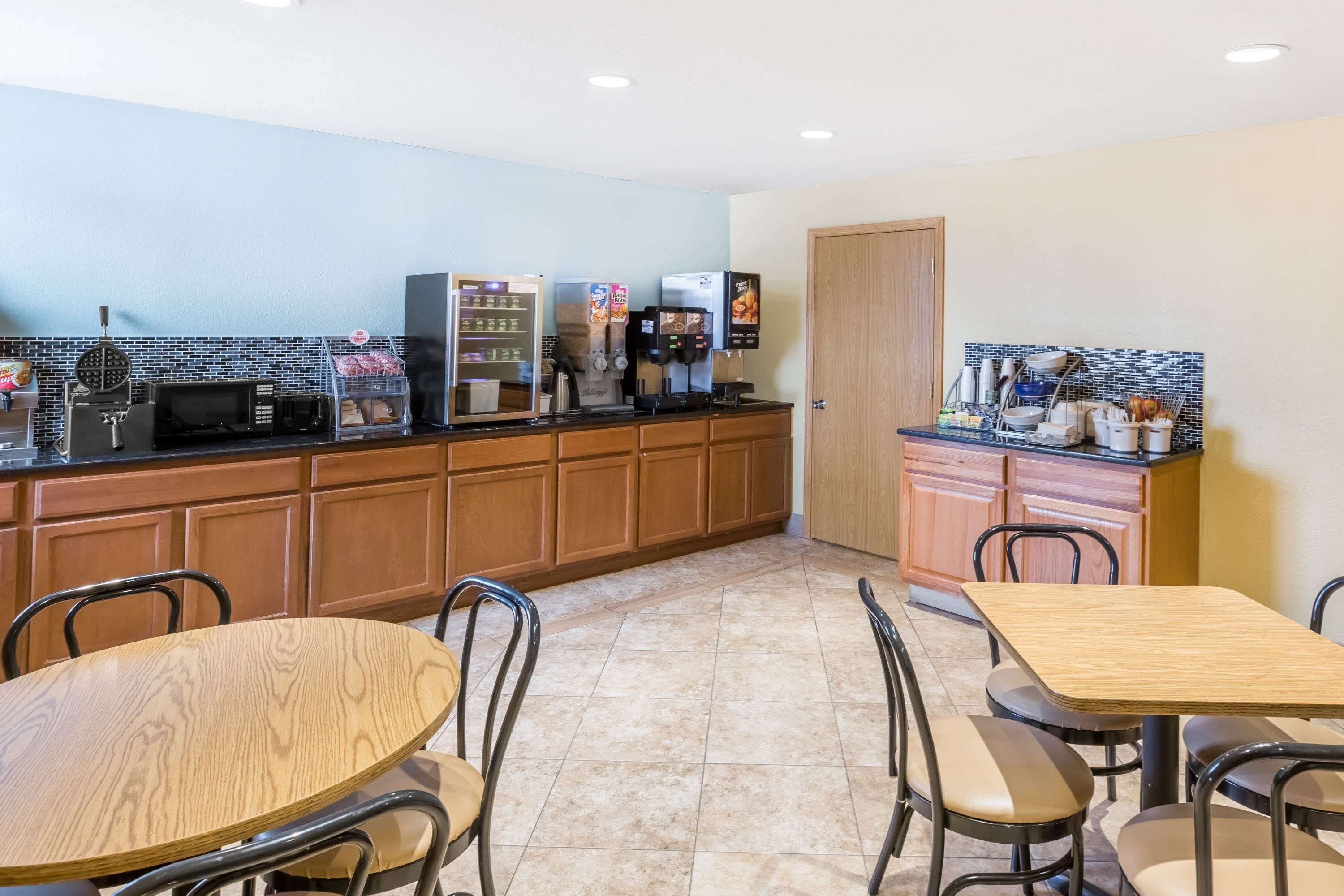 A kitchen with wooden cabinets, a microwave, a coffee machine, and a toaster. There are chairs and a table in the dining area.