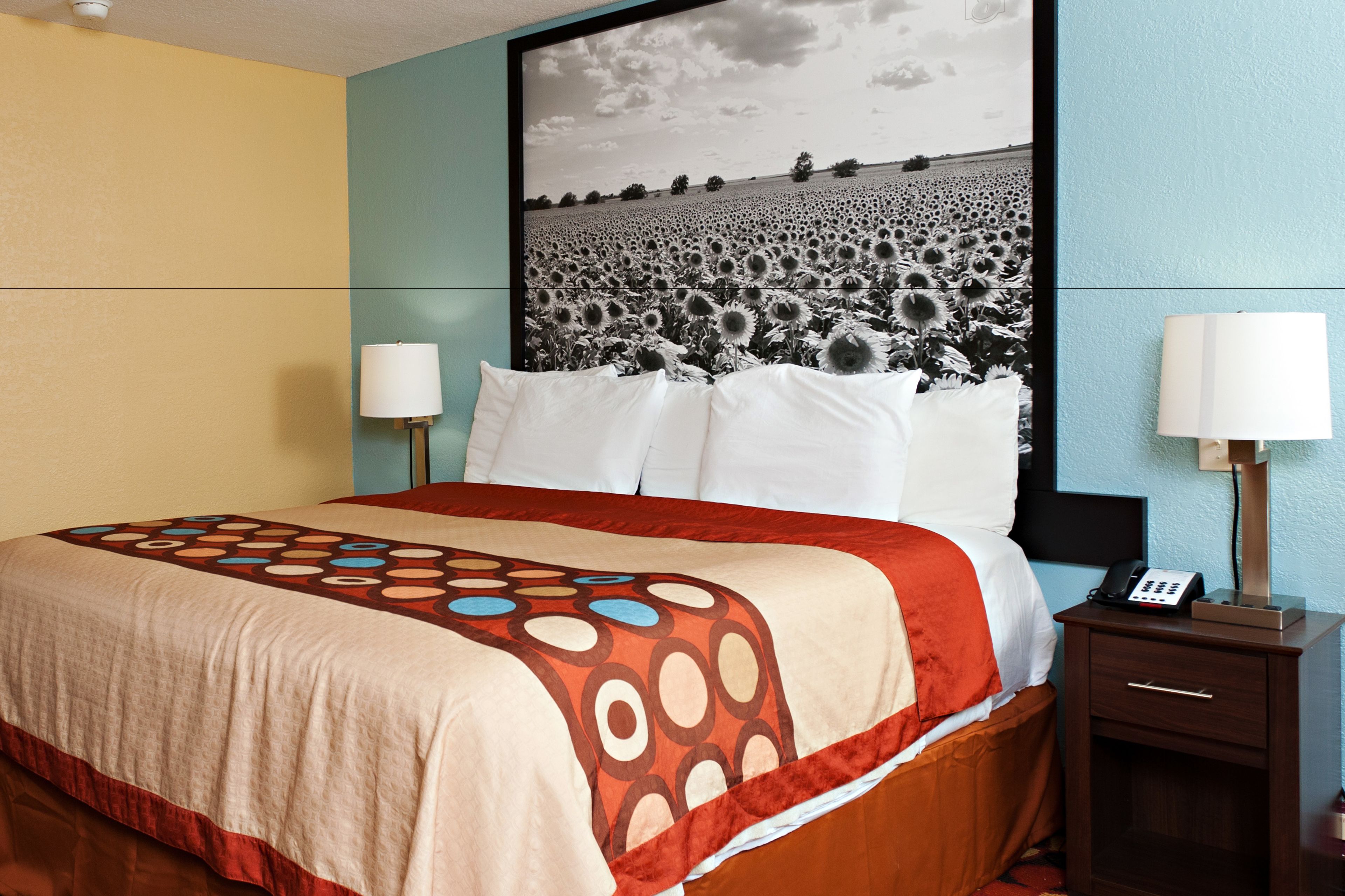A hotel room with a large bed, a nightstand with a phone, and a wall-mounted lamp.