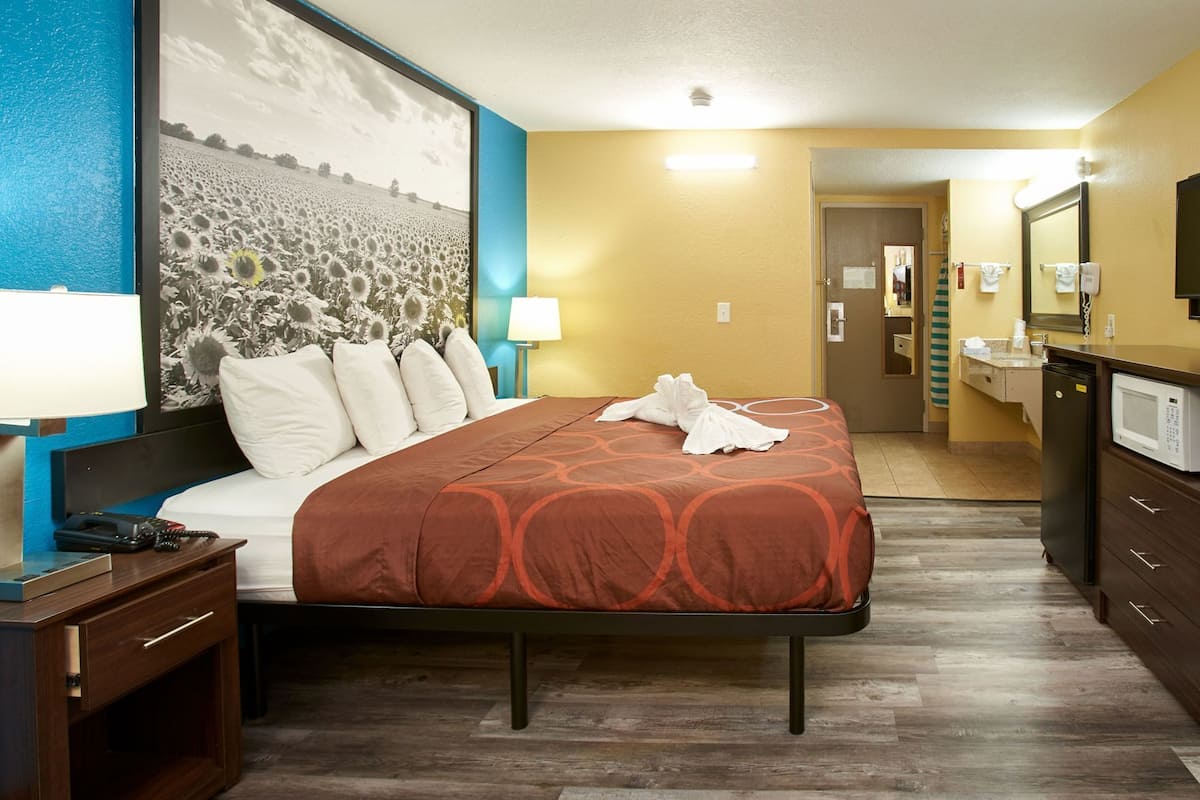 A hotel room with a bed, a nightstand, a desk, a microwave, and a bathroom visible through an open door.