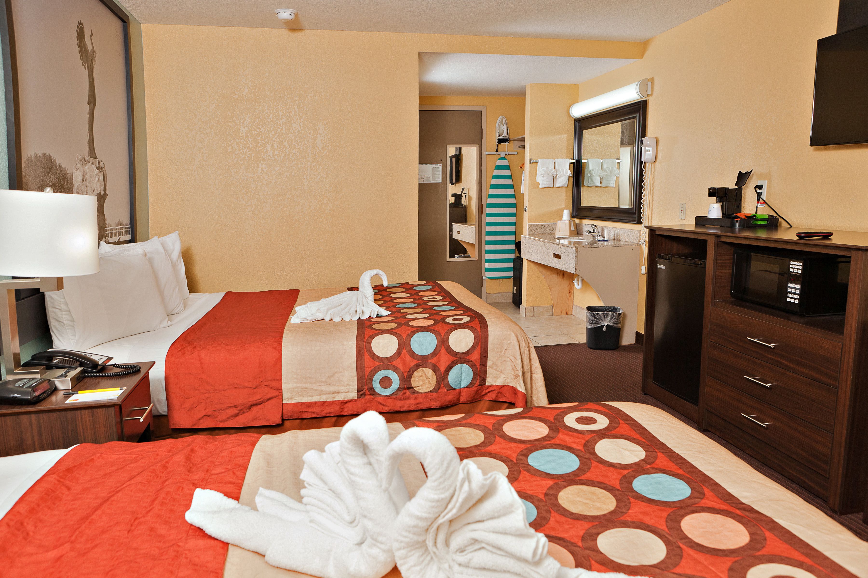 Habitación de hotel con dos camas, un escritorio, teléfono, espejo y televisión.