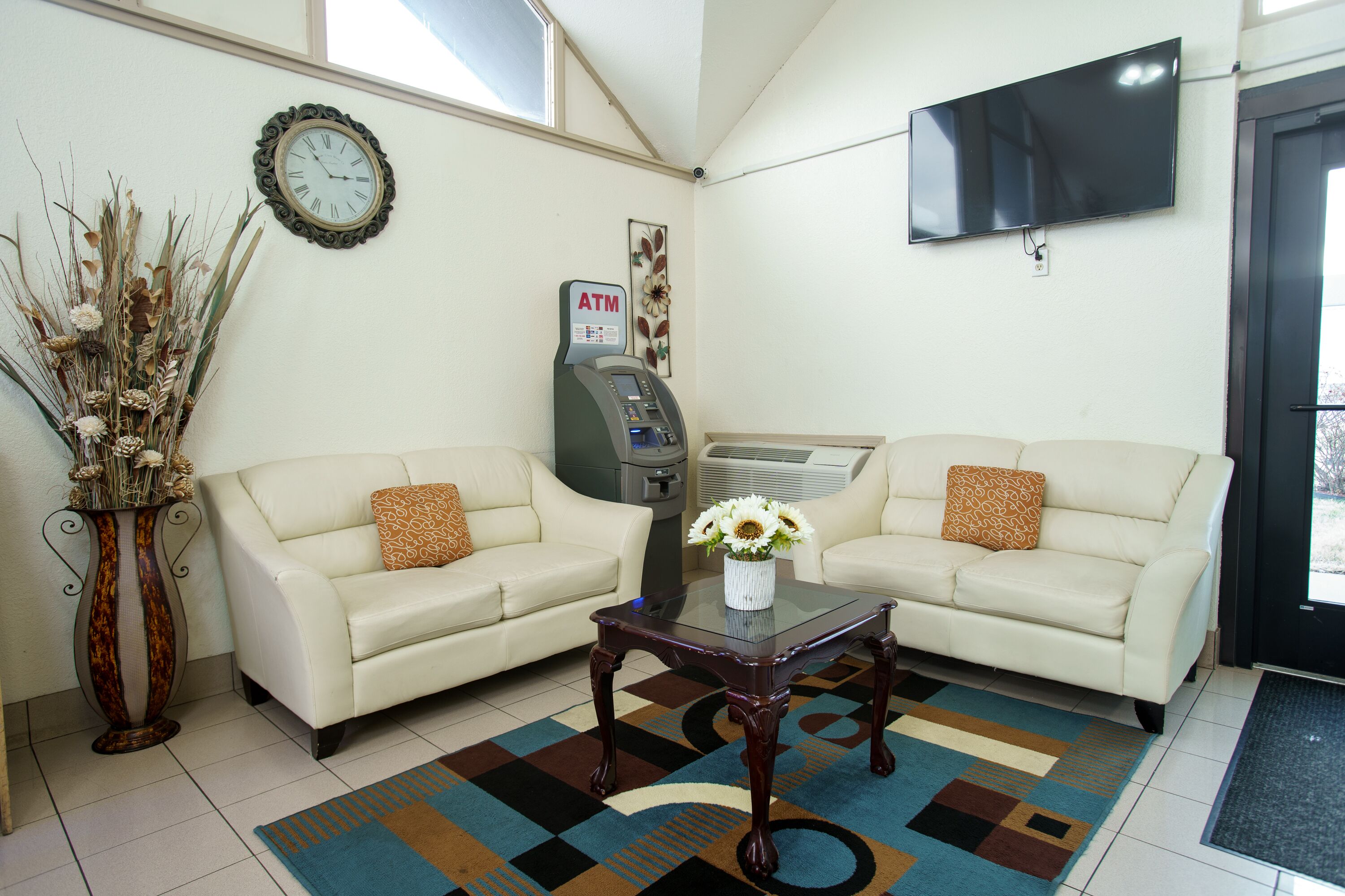A hotel lobby with two sofas, a coffee table, an ATM, and a TV mounted on the wall.