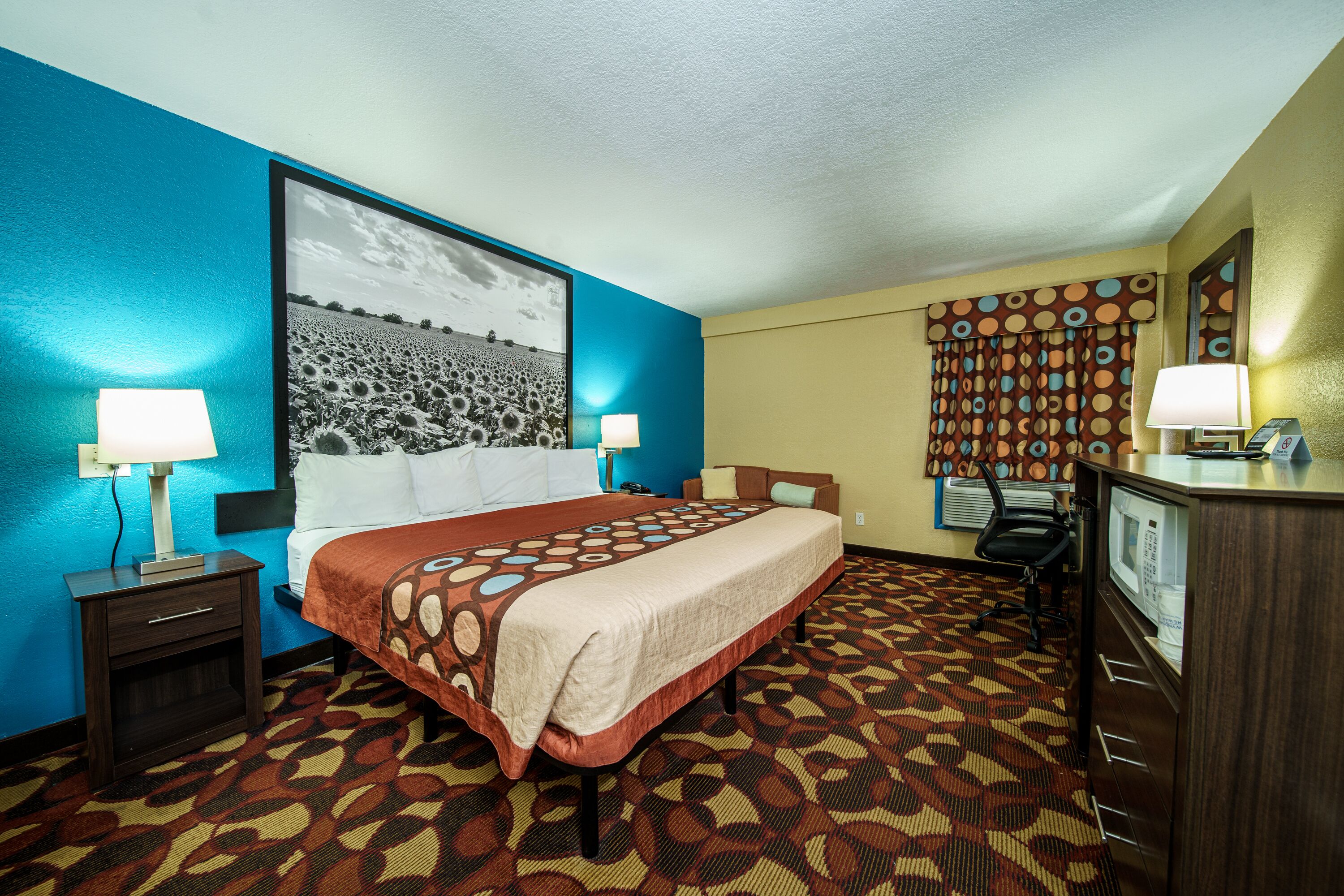 A hotel room with a large bed, two bedside tables with lamps, a desk with a computer, and a patterned carpet.