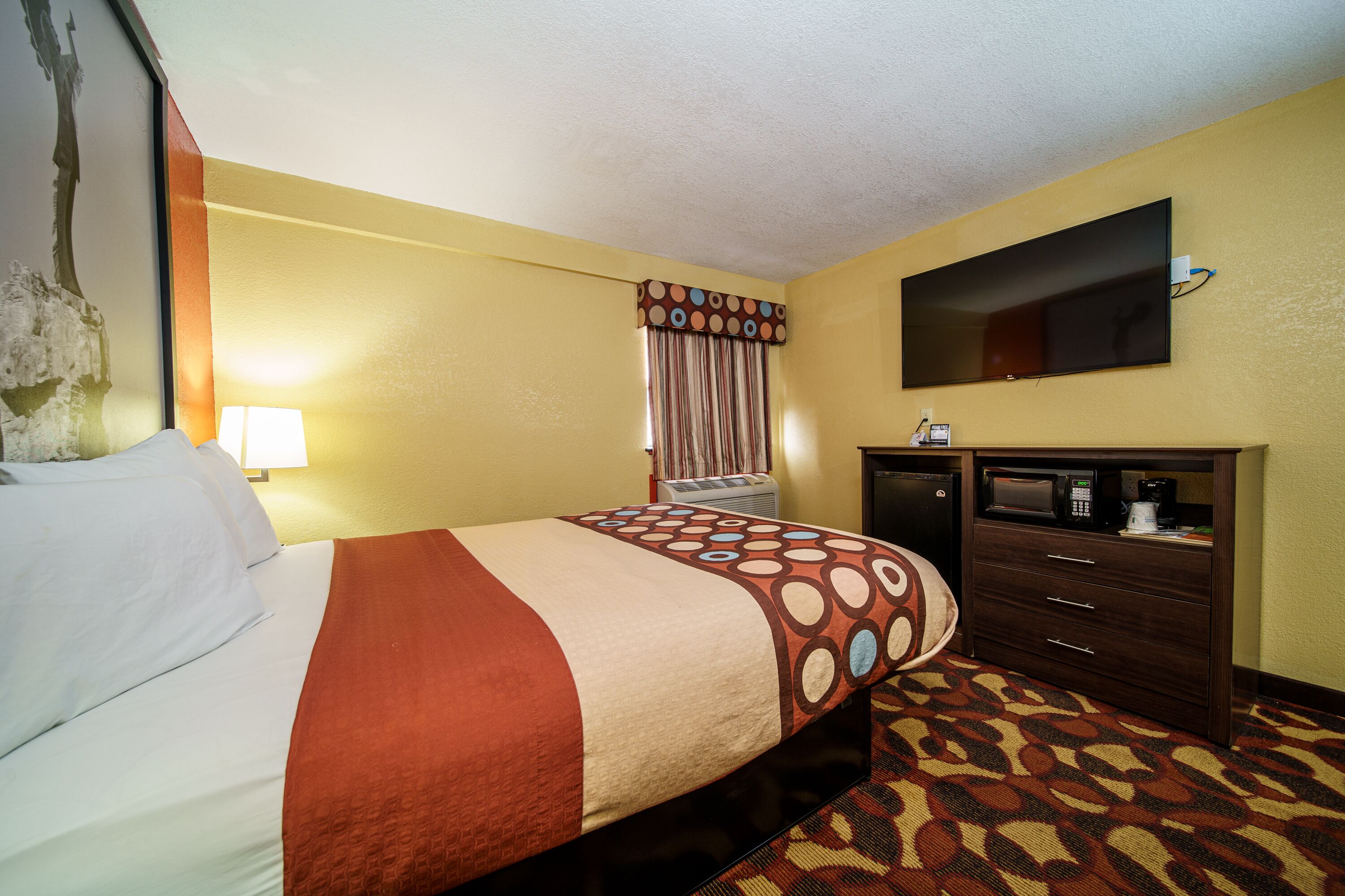 A hotel room with a bed, a dresser, a television, and a window with curtains.