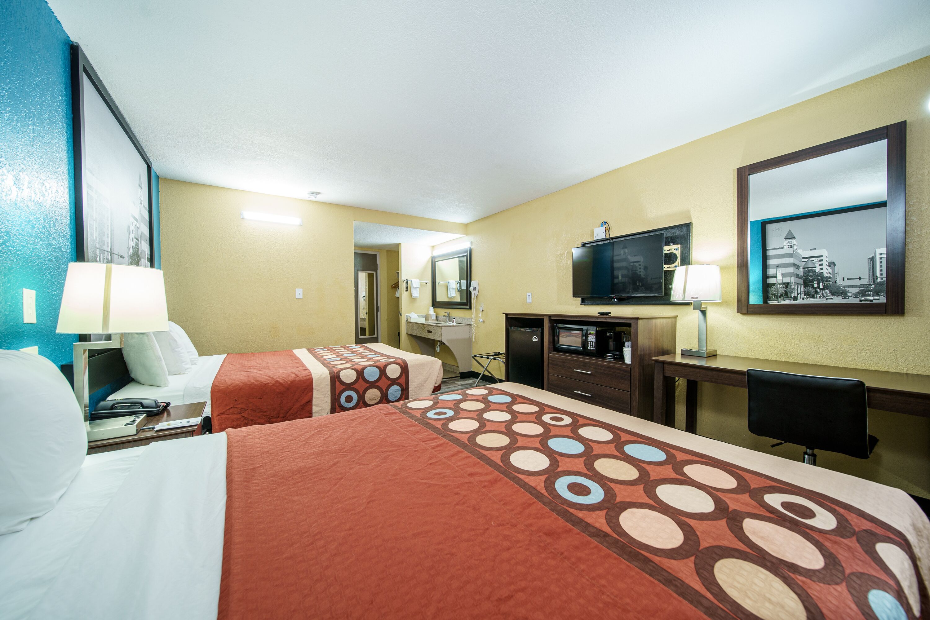 A hotel room with two beds, a desk, a television, and a bathroom visible through an open door.