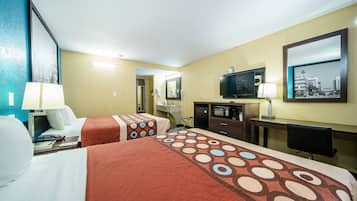 Habitación de hotel con dos camas, un escritorio, televisor y baño visible a través de una puerta abierta.