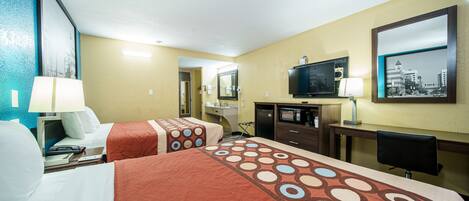 A hotel room with two beds, a desk, a television, and a bathroom visible through an open door.