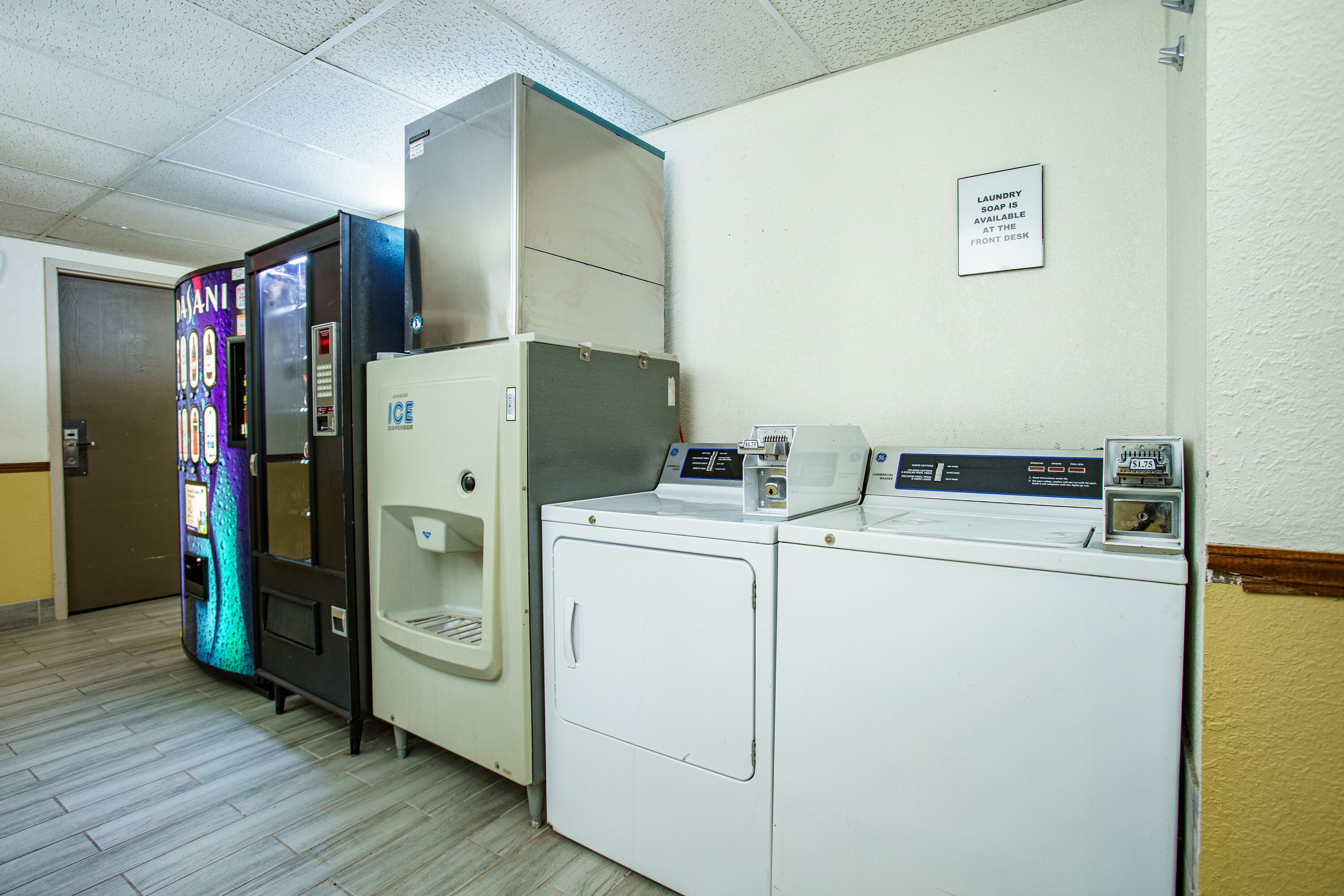 A laundry facility with a vending machine, a water cooler, and a sign indicating the availability of laundry soap at the front desk.