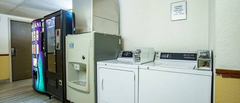 A laundry facility with a vending machine, a water cooler, and a sign indicating the availability of laundry soap at the front desk.