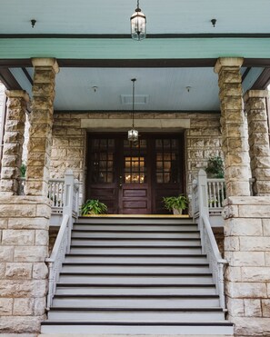 A stone building with a porch, a set of stairs, and a hanging lantern. - The Mansion at Elfindale (Springfield)