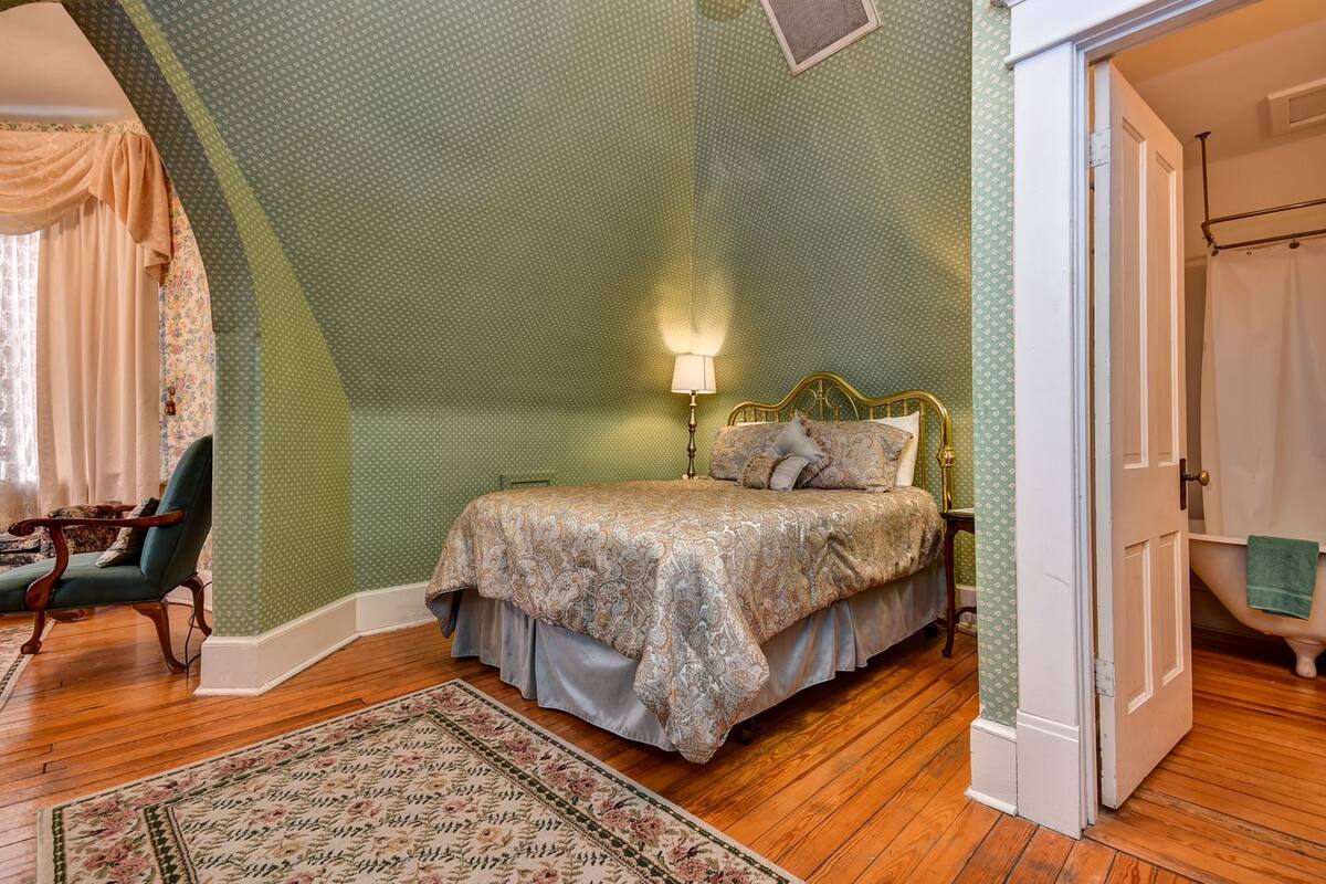 A bedroom with a bed, a chair, a nightstand, and a green patterned wall.