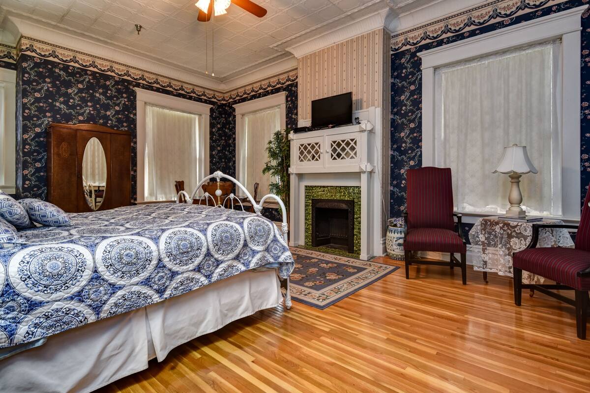 A bedroom with a bed, a fireplace, a television, and a desk with a chair.