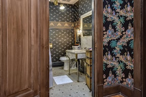 Un baño con inodoro, lavabo y espejo. Las paredes tienen un papel tapiz estampado.