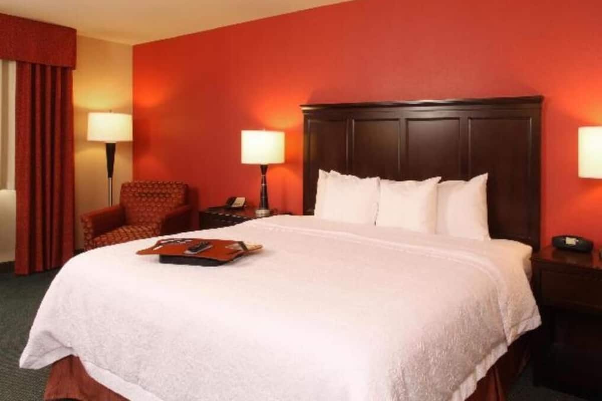 A hotel room with a large bed, two bedside lamps, a chair, and a nightstand.