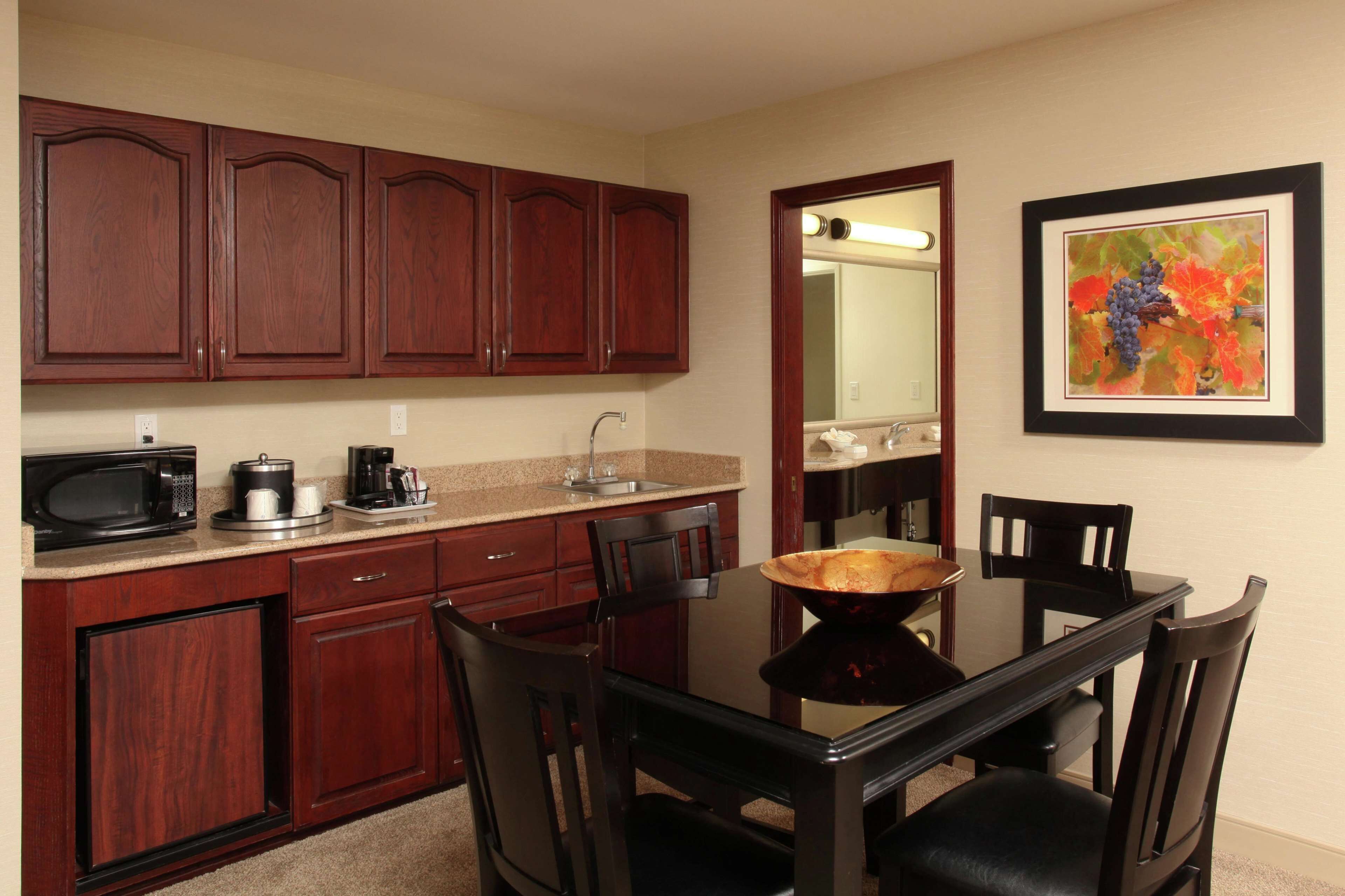 Cocina compacta con armarios de madera, microondas, cafetera y una mesa de comedor con sillas.