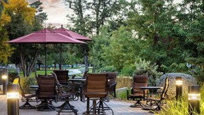 An outdoor patio with tables and chairs, surrounded by trees and greenery. - Hampton Inn Richland/Tri-Cities (Richland)