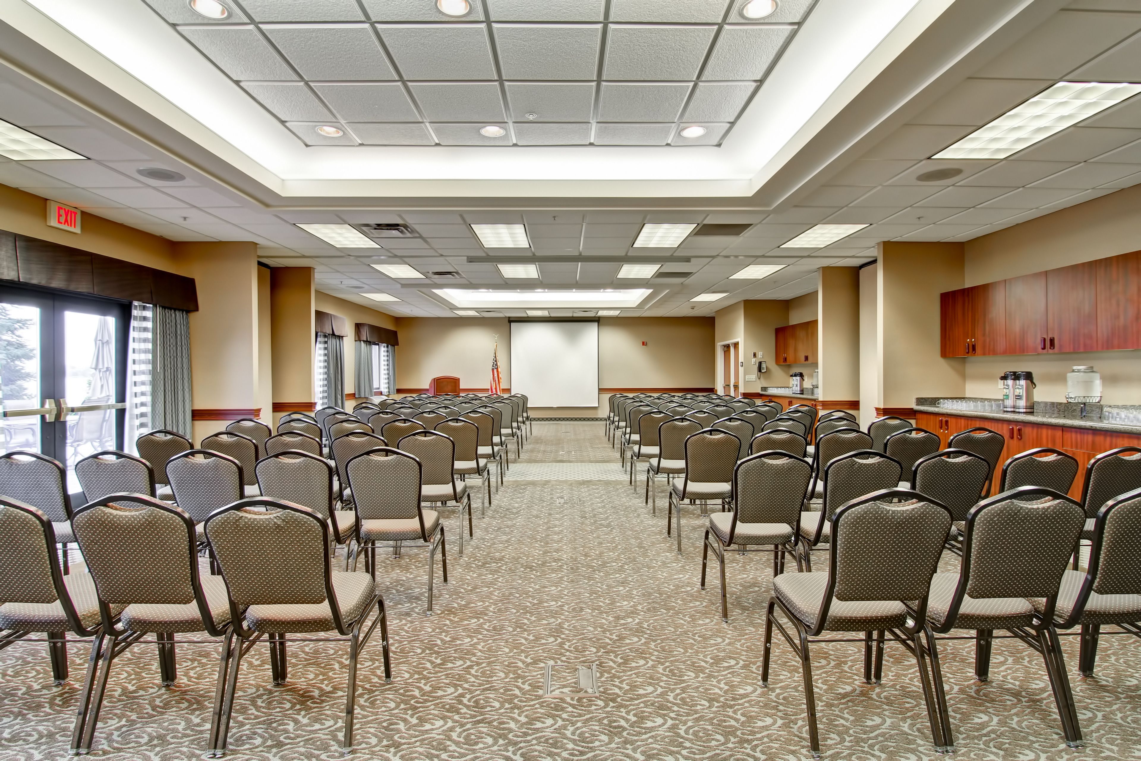Une salle de conférence avec des rangées de chaises, un pupitre et un écran de projection.