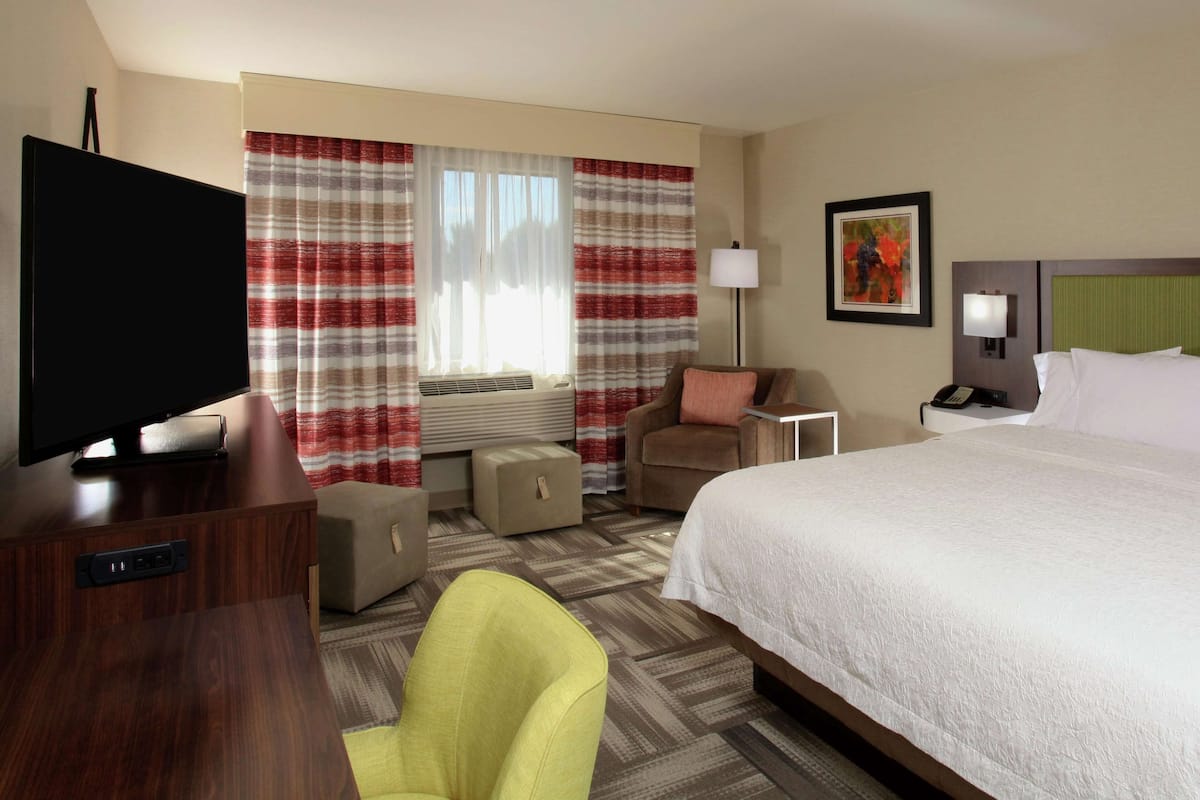A hotel room with a bed, a television, a chair, a desk, and a lamp.
