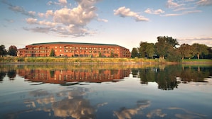 A large, multi-story building with a flat roof, situated by a calm body of water reflecting the structure. - Hampton Inn Richland/Tri-Cities (Richland)
