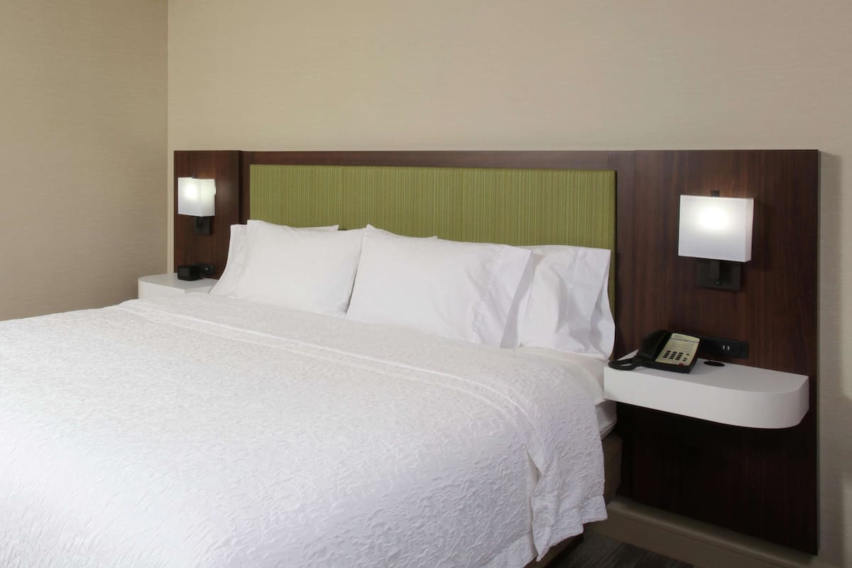 A hotel room with a large bed, two bedside lamps, a nightstand with a phone, and a green headboard.