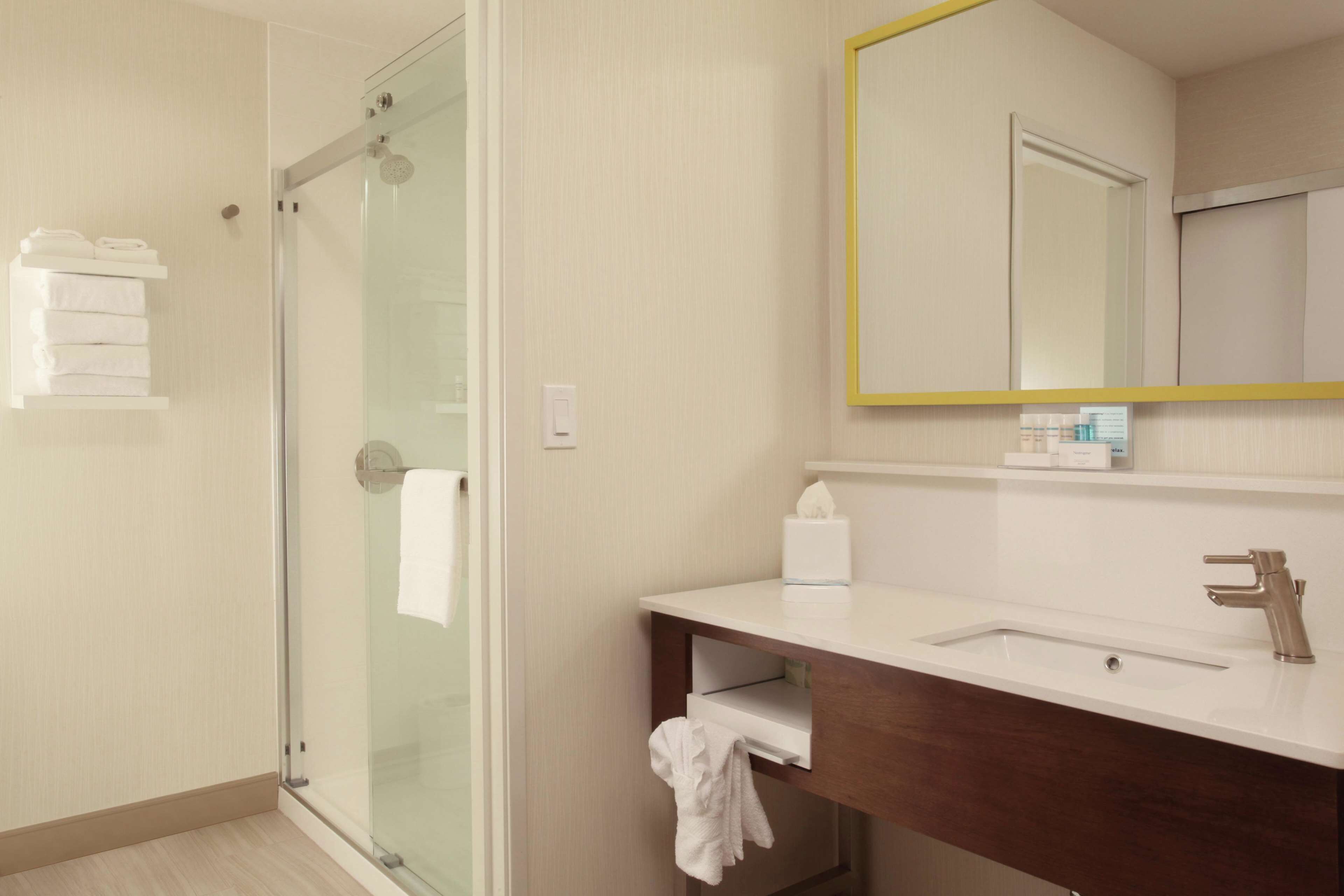 A modern bathroom with a glass shower enclosure, a white sink with a wooden vanity, and a mirror with a yellow frame.