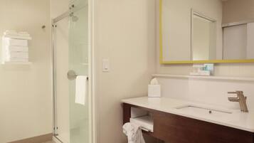 A modern bathroom with a glass shower enclosure, a white sink with a wooden vanity, and a mirror with a yellow frame.