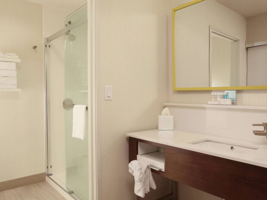 A modern bathroom with a glass shower enclosure, a white sink with a wooden vanity, and a mirror with a yellow frame.
