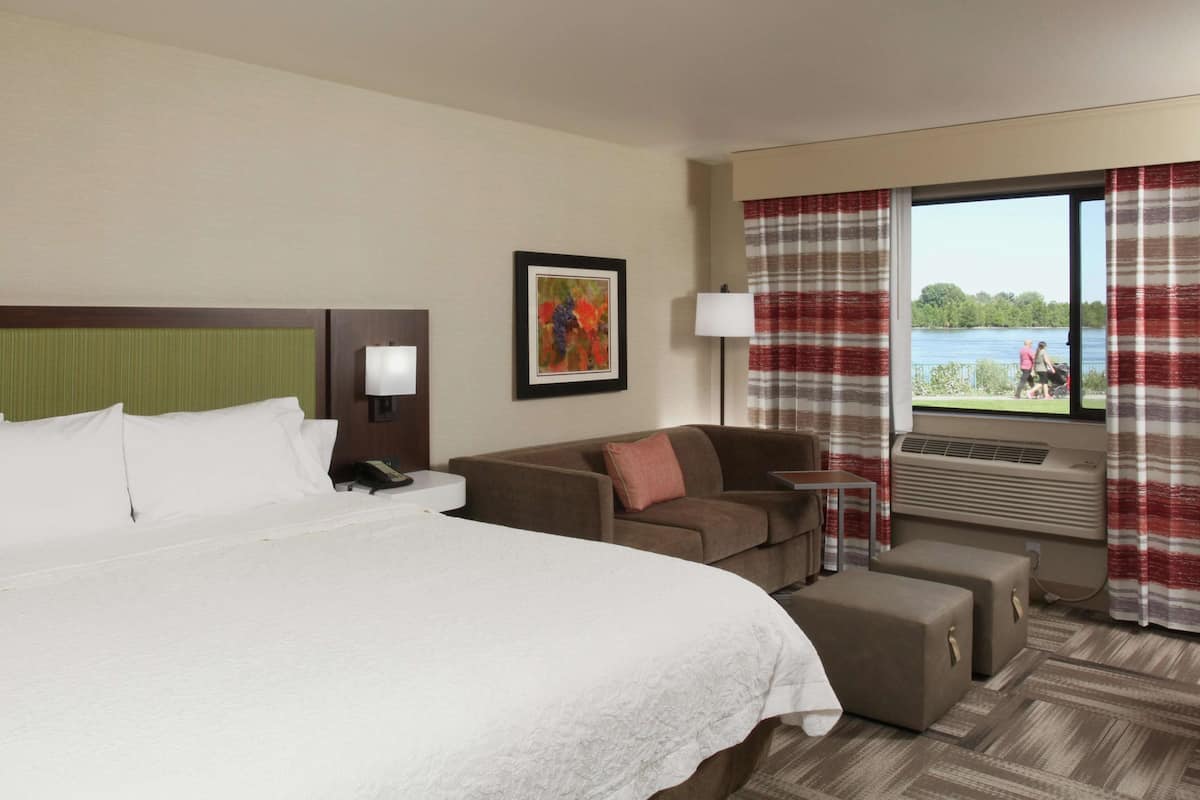 A hotel room with a large bed, a sofa, a small table, and a window with curtains.