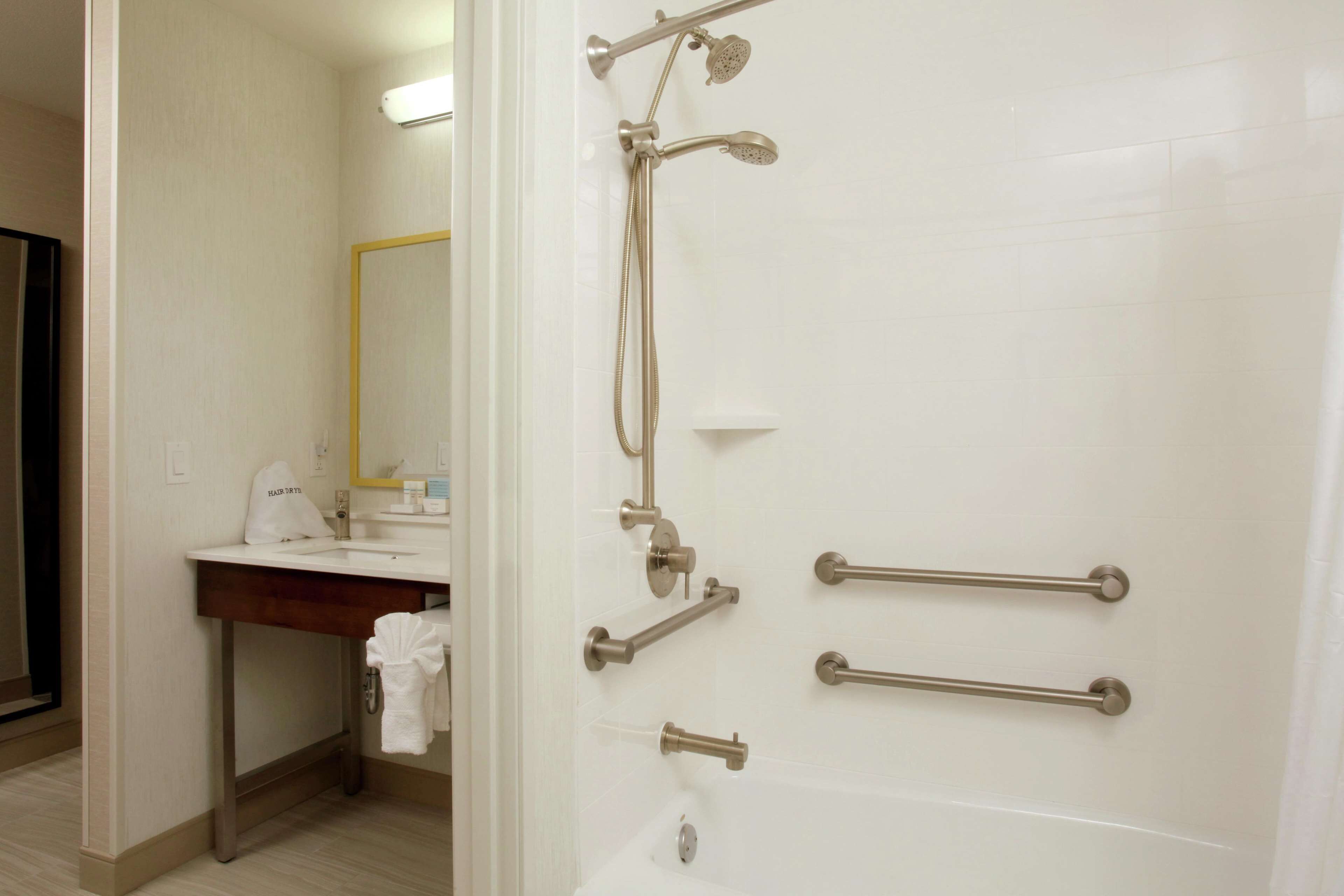 A bathroom with a white sink, mirror, and shower with grab bars.
