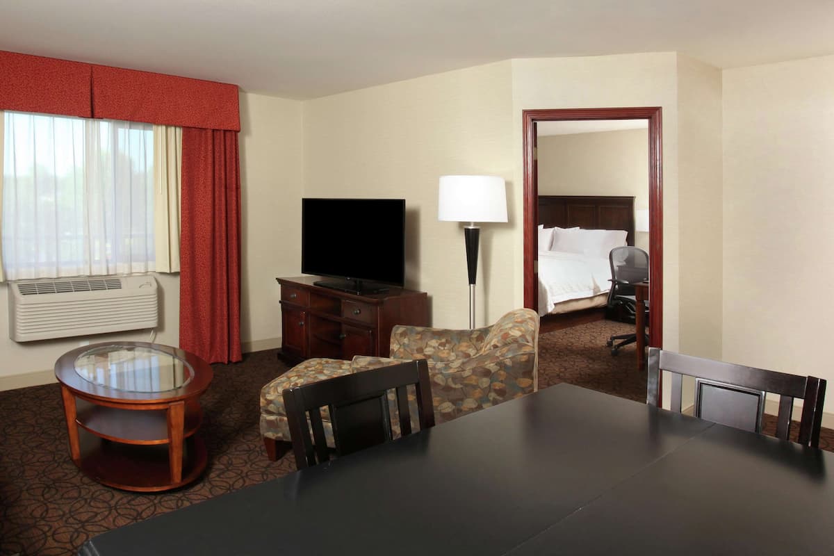 A hotel room with a bed, a TV, a desk, a chair, a lamp, and a window with curtains.