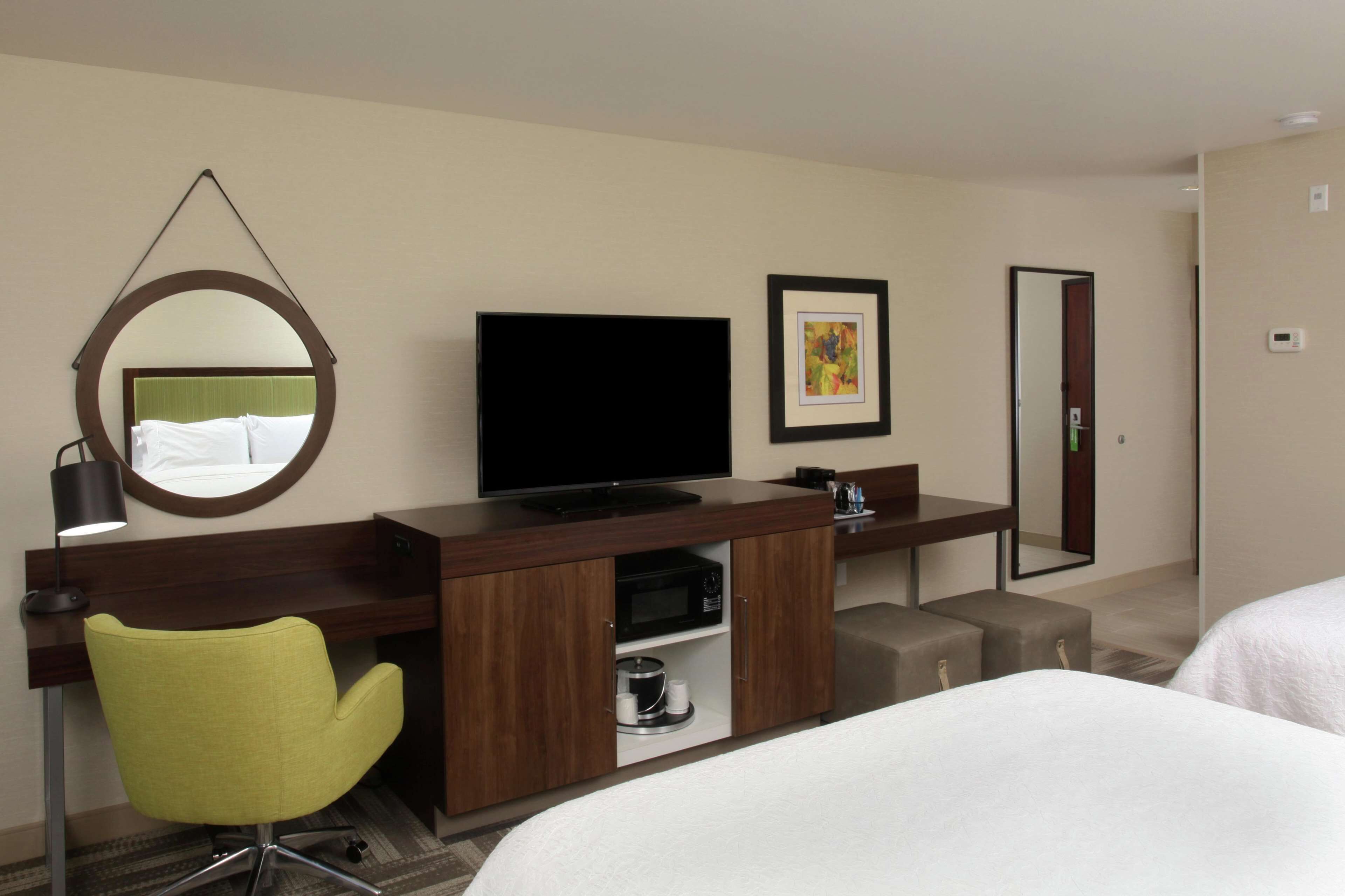 Habitación de hotel con una cama, un escritorio con televisión, una silla, microondas y un cuadro en la pared.